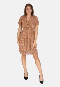 Vestido envolvente marrón con estampado floral, de mangas cortas y cintura ceñida, confeccionado en una tela ligera y texturizada. Combinado con tacones altos negros.