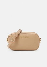 Mala tiracolo em pele bege com fecho de correr, alça ajustável e detalhes do logótipo em dourado. Textura suave e formato oval com bordas arredondadas.