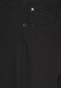 Tmavě černé džínové kalhoty s texturovaným povrchem, přičemž mají přední kapsu a stříbrné kovové doplňky. Šití podél švů.