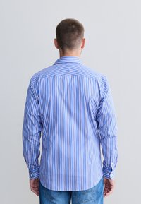 Košulja s dugim rukavima u plavoj boji s uspravnim bijelim i ružičastim prugama, s ovratnikom i manšetama s gumbima, izrađena od glatkog materijala.