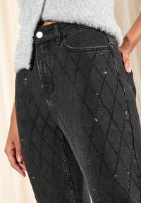 Čierne džíny z denimu s diamantovým vzorom, zdobené rhinestone; majú predné vrecká a klasický pás s gombíkovým zapínaním.