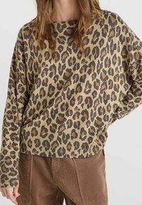 Femme portant un pull ample à motif léopard assorti d'un pantalon en velours côtelé marron taille haute, sur un fond uni.