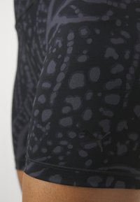 Close-up of dark patterned athletic shorts with subtle Puma logo on the thigh, worn on a person's leg.