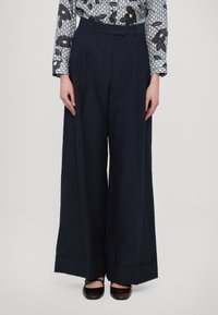 Námornické široké kalhoty s texturovaným vzorem, vysokým pasem, předními záhyby a detailním ohnutím nohavic. Doplněné tmavými botami.