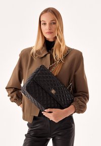 Borsa a spalla nera trapuntata con un accento in oro e tracolla a catena, caratterizzata da una forma rettangolare e una superficie liscia.
