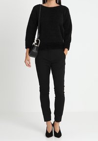 Pull noir en mohair à col rond, associé à un pantalon noir ajusté et des escarpins noirs, accessoirisé d'un petit sac bandoulière.