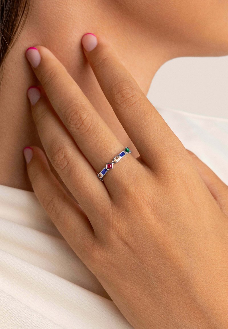 Anillo de plata con múltiples piedras preciosas en rojo, azul, verde y amarillo, con un diseño geométrico sobre una banda delgada.