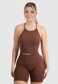 Bruine geribde sportset met een halternek crop top en high-waisted shorts met textuurpaneel details. Rekbare, nauwsluitende pasvorm.