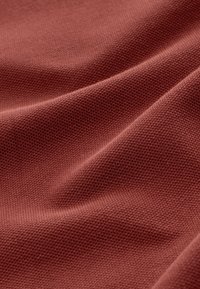 Tela texturizada, color granate, patrón tejido, apariencia suave, con pliegues y arrugas visibles, mostrando textura y profundidad detalladas.