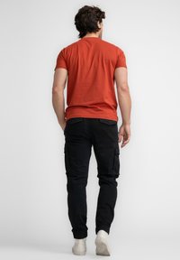 Rode katoenen t-shirt met korte mouwen, gecombineerd met zwarte cargobroek met zijzakken. Model draagt witte sneakers.