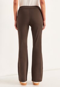 Braune Schlaghosen mit glatter Textur und elastischem Bund. Sie haben einen langgezogenen Schnitt mit geraden Nähten und keine sichtbaren Taschen oder Verzierungen.