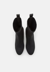 Schwarze gestrickte Knöchelstiefel mit vertikal gerippter Textur, runder Zehenpartie und Ziehschlaufe an der Rückseite, versehen mit einem glatten Innenfutter.