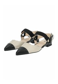 Zapatos planos de punta afilada con un upper beige y puntera de cuero negro, que presentan una correa elástica negra y acentos de hardware plateado.