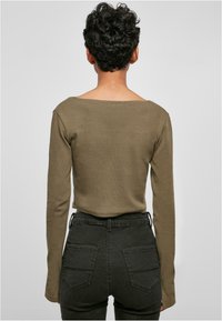Olivegrünes Langarmoberteil mit weitem Rundhalsausschnitt, kombiniert mit dunklen, hoch geschnittenen Jeans aus Denim mit Gesäßtaschen und schlankem Schnitt.