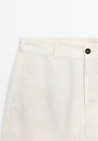Lichtbeige linnen broek met een gladde textuur, voorzien van een zwarte knop, riemlussen en zijzakken voor functionaliteit.