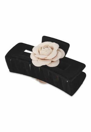 Zwarte fluwelen haarclutch met een lichtbeige vilten bloemenaccent, met een rechthoekige vorm en een geperforeerd ontwerp voor grip en stijl.