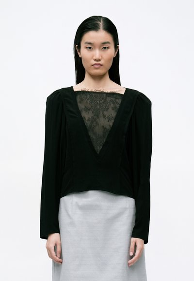 Blusa negra de mangas largas, con un escote en V profundo y un panel de encaje transparente. Falda gris texturizada completa el conjunto. Tejido suave.