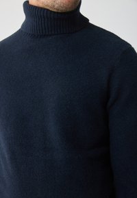 Námornícky modrý rolák vyrobený z jemnej, textúrovanej látky. Má rebrovaný golier a priliehavý strih, vhodný na vrstvenie v chladnom počasí.