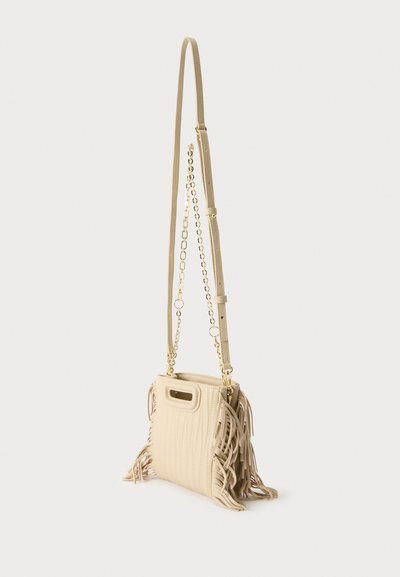 Sac bandoulière beige avec longue sangle réglable, détail chaîne dorée, poignée découpée et accents à franges sur les côtés.