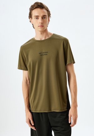 Oliven grøn kortærmet træningsshirt lavet af glat, letvægts materiale. Har rund halsudskæring og trykt tekst i sort: "STOP IKKE FØR DU ER STOLT."