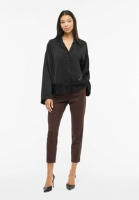 Svart satengbluse med krage og frontknapper, med en teksturert blonderkant nederst. Kombinert med skreddersydde brune bukser og hæler.