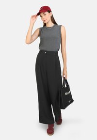 Gray sleeveless top, high-waisted black wide-leg pants, red sneakers, and a maroon cap with white text. Black tote bag with white lettering.
