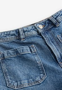 Modré džíny z denimu s viditelnou zadní kapsou, zdobené oranžovým prošíváním a kovovým zapínáním v pase.