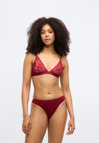 Burgundzki komplet bielizny składający się z koronkowego biustonosza z kwiatowymi wzorami i cienkimi regulowanymi ramiączkami, połączony z pasującymi, niskim stanem figami.