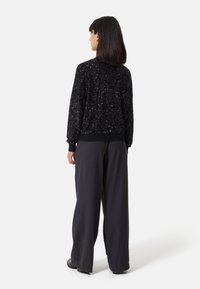 Maglione nero con paillettes, dalla vestibilità comoda, con polsini e orlo a coste; abbinato a pantaloni grigi larghi. Texture liscia con dettagli luccicanti.
