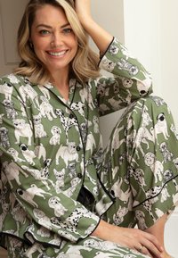 Groene pyjama set met verschillende hondillustraties in zwart-wit, met contrasterende zwarte afwerking en knopen. Zachte stoftextuur.