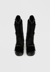 Črne gležnjarje iz umetnega krzna s gladkim zgornjim delom iz črne usnjene in srebrnimi sponkami, ki imajo debel črn podplat.