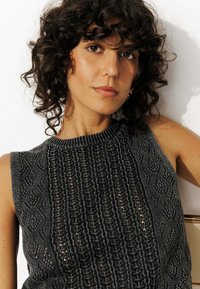 Haut en tricot noir avec un motif texturé comprenant des rayures verticales et des formes de diamant. Encolure festonnée, design sans manches.