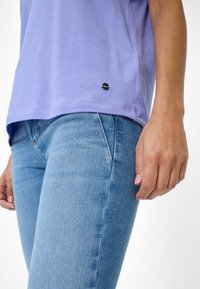 Lyse lilla bomulds t-shirt med korte ærmer og et lille sort logo mærke, parret med blå denim jeans der har en tætsiddende pasform.