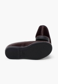 Zapato de terciopelo marrón oscuro con punta redondeada, suela de goma negra y detalles de costura sutiles. Textura suave y un diseño sencillo.
