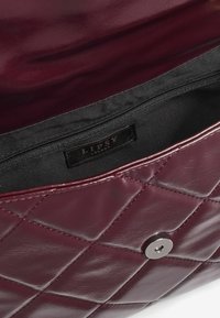 Borsa in pelle bordeaux trapuntata con fermaglio magnetico argento e interno in tessuto nero, dotata di una tasca con zip e etichetta Lipsy London.