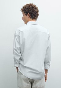 Lichtgrijze langemouwen shirt met een relaxte pasvorm, zichtbare naden en een rugpand, gecombineerd met lichtgekleurde broeken. Zachte stoftextuur.