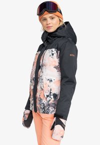 Roxy ski jacket featuring a black and floral pattern in pink and gray tones, with a zip front and attached hood, paired with matching mittens.