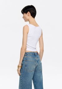 Witte geribbelde tanktop met een ronde hals, gecombineerd met losse blauwe denim jeans met een vervaagde wassing en minimale stikdetails.