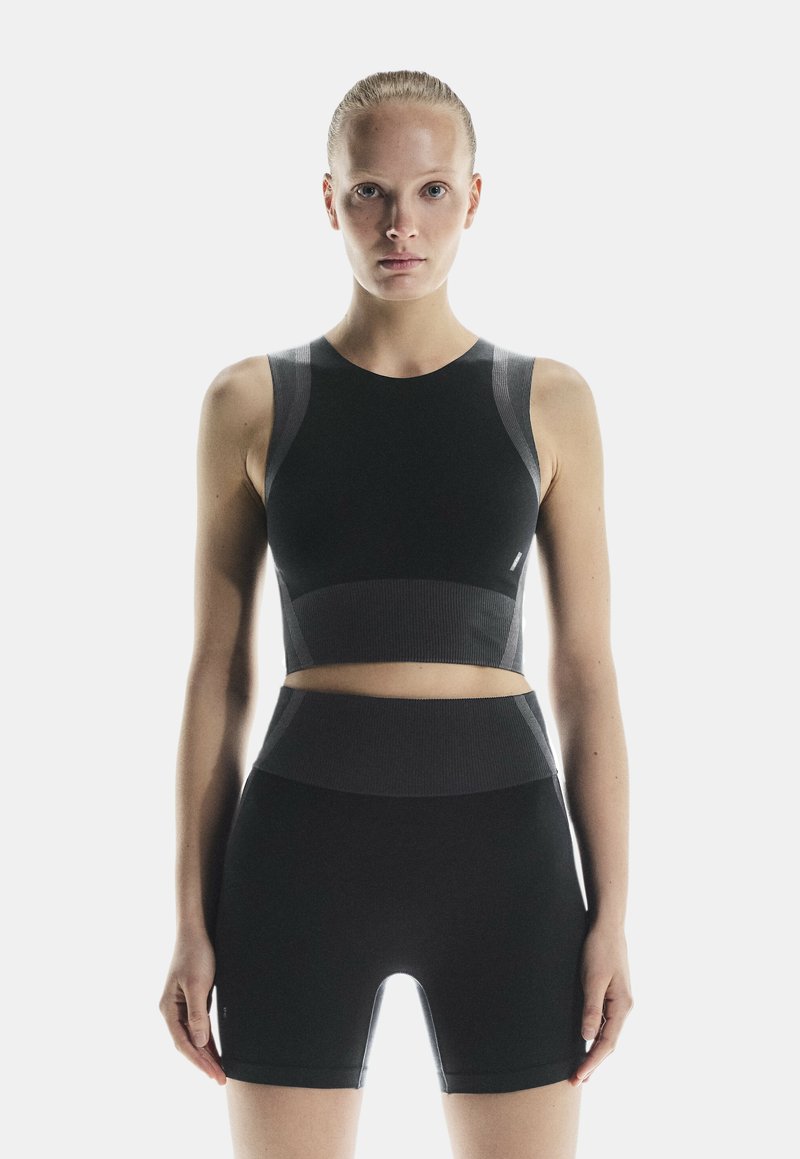 Ensemble de sport noir comprenant un top court avec des accents côtelés et un short taille haute. Texture lisse et design ajusté.