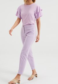 Světle fialové tričko s volánkovými rukávy, v kombinaci s upravenými světle fialovými kalhotami s přední kapsou a zapínáním na knoflík.