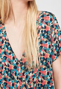 Blusa de estampado floral en vibrantes colores rojo, teal y negro. Presenta un escote en V profundo y mangas cortas sueltas. Tejido suave y liviano.