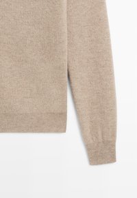 Beżowy sweter z miękkiej dzianiny; posiada długie rękawy, prążkowane mankiety i dół oraz gładką fakturę. Brak widocznych wzorów i ozdób.