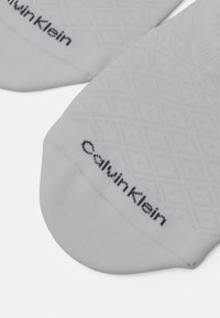 Pilki medvilniniai kojinės su tekstūruota deimanto raštu ir juodu atspaudu „Calvin Klein“ logotipo šalia krašto.