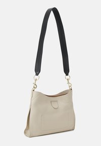 Beżowa skórzana torba na ramię z czarnym paskiem, złotymi akcesoriami, jedną zewnętrzną kieszenią i miękkim, teksturowanym wykończeniem.