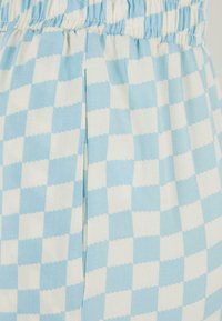 Tissu à carreaux bleu clair et blanc avec une texture douce. Présente une taille élastique et un détail de couture sur le côté.