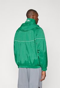 Grøn vindjakke med hætte, elastiske manchetter og kant, hvide accenter og "Celtics" broderet på kraven.