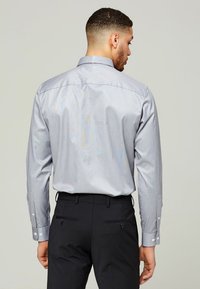 Knapp-up skjorta i ljusgrått med ett subtilt randigt mönster, långa ärmar och vita knappar; parat med mörka byxor.