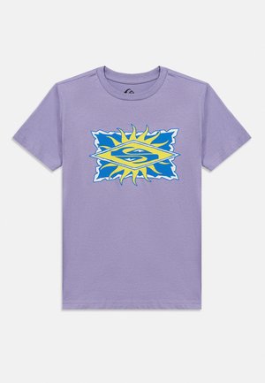 Lila rövid ujjú, kerek nyakú póló középen egy sárga nap grafikájával és kék háttérrel, amelyen stilizált „S” embléma látható.