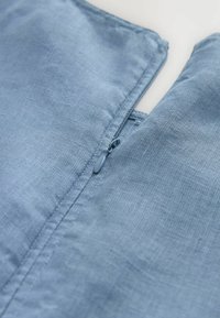 Tessuto di lino blu con una chiusura a cerniera discreta, che mette in evidenza una superficie liscia e linee semplici e pulite.