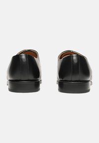Chaussures de ville en cuir noir avec une finition lisse, embouts ronds et un petit talon empilé. Détails de couture mineurs près du talon.